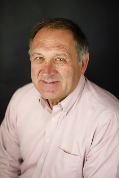 Brad Johnston poses sitting wearing a white oxford shirt embroidered with the Hometown Realty logo